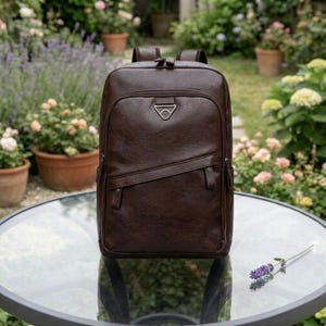 Può includere: Uno zaino in pelle marrone con una tasca frontale e una cerniera diagonale. Lo zaino ha una maniglia superiore e spallacci regolabili. Lo sfondo mostra un giardino con fiori e piante.