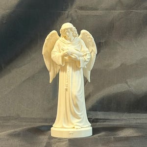 May include: A cream-coloured angel figurine with outstretched wings, holding a dove. The angel is wearing a long robe and has a serene expression. The statue is standing on a round base.