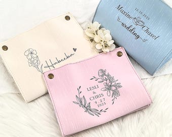 May include: Four personalized catch-all trays in cream, pink, and blue. Each tray features a unique design and text, including floral illustrations and names with dates. The trays are fastened with brass-colored snaps.