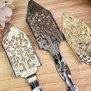 Könnte beinhalten: Drei verzierte Absinthlöffel in Silber, Gunmetal und Gold. Jeder Löffel hat ein dekoratives, durchbrochenes Design und einen Griff. Der goldene Löffel ist mit dem Namen "Daniel" graviert.