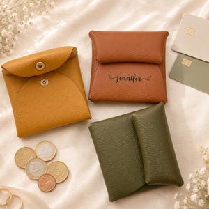 May include: An assortment of leather coin purses in mustard yellow, brown, and olive green. The brown purse is personalized with the name "Jennifer". Euro coins, credit cards, and floral accents complete the scene.