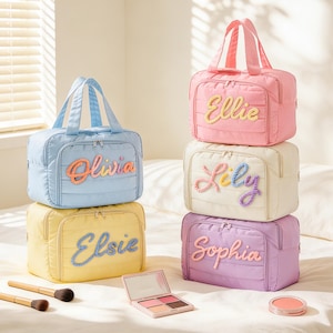 Puede incluir: Una colección de cinco neceseres acolchados rectangulares con asas superiores y cierres de cremallera. Cada bolsa presenta un nombre bordado en hilo de colores: Olivia, Elsie, Ellie, Lily y Sophia. Se incluyen dos brochas y un estuche de maquillaje.