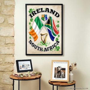 Puede incluir: Una impresión enmarcada con un trébol verde y una bandera sudafricana cruzada sobre una bandera irlandesa. El texto "IRELAND" y "SOUTH AFRICA" está impreso en negro sobre un fondo blanco.