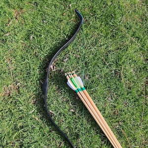 May include: A black recurve bow with a blue string and a bundle of wooden arrows with green fletching.