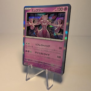 May include: A holographic Pokémon trading card featuring Mewtwo, displayed on a clear acrylic stand. The card has a purple background with Japanese text and a 3D effect. The card's HP is 130.
