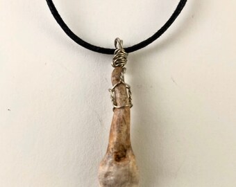 May include: A bone pendant necklace with a wire wrap. The pendant is a long, thin bone with a rounded end. The necklace is made of black cord.