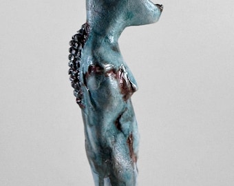 May include: A blue ceramic sculpture of a stylized animal form, suspended by a black cord. The sculpture has a textured surface with dark brown accents and a dark, textured spine. The overall shape is elongated and organic.