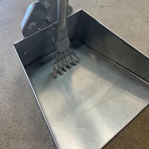 May include: A metal dustpan with a handle and a rake-like attachment. The dustpan is rectangular with a flat bottom and sides. The handle is attached to the dustpan at an angle. The rake has several curved tines.