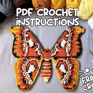 Op de afbeelding: Een gehaakte vlinder in tinten oranje, geel, bruin en wit, met de tekst "PDF Crochet Instructions" en "Frantic Crochet". De afbeelding bevat garen, een haaknaald en een schaar, wat wijst op een knutselproject.