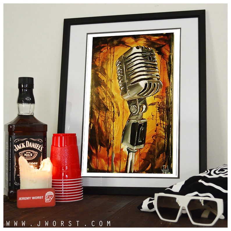 May include: A framed painting of a vintage microphone with a yellow, orange, and brown background. The microphone is silver and has a black stand. The painting is framed in black and has a white mat.