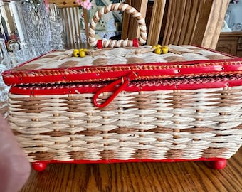 May include: A woven wicker storage box with a red lid and a red handle. The box has a red and white checkered pattern on the lid and yellow beads on the handle.