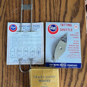 May include: Vintage Boye crochet and tatting tools, including a crochet fork, tatting shuttle, and Crazy-Daisy winder. The crochet fork is 1 inch wide. The tools are displayed on a wooden surface.