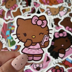 Può includere: Un adesivo in vinile fustellato raffigurante un personaggio gatto dei cartoni animati marrone con un fiocco rosa, che indossa un vestito a quadri rosa e tiene in mano uno smartphone rosa. Il personaggio ammicca, ha baffi neri e un naso giallo.