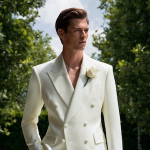 May include: Cream double-breasted suit with a white rose buttonhole. The suit has a notched lapel and a classic fit. The text "Chic Prime" is visible. The background features green foliage and a blue sky.