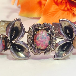 May include: A silver bracelet with three pink opal stones set in a floral design. The bracelet has a chain link closure.