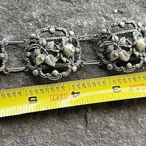 May include: A silver bracelet with a floral design. The bracelet is 4 inches long and has a clasp.