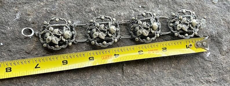 May include: A silver bracelet with a floral design. The bracelet is 4 inches long and has a clasp.