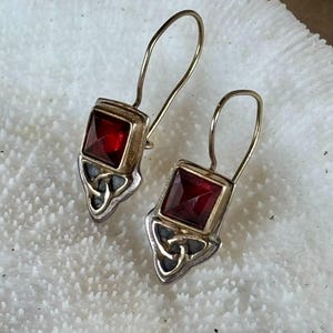 May include: A pair of silver earrings with a red gemstone and a Celtic knot design.