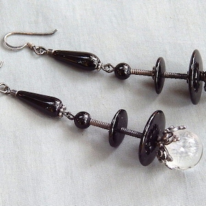 May include: A pair of silver earrings with black and clear glass beads. The earrings feature a teardrop-shaped bead, a round bead, and a clear glass orb.