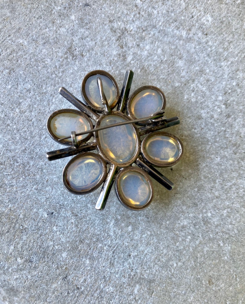 K&ouml;nnte beinhalten: Eine silberne Brosche mit einem Blumendesign mit acht wei&szlig;en Opal-Steinen.