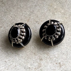 May include: A pair of black onyx earrings with silver accents. The earrings are round and have a beaded design around the edge.