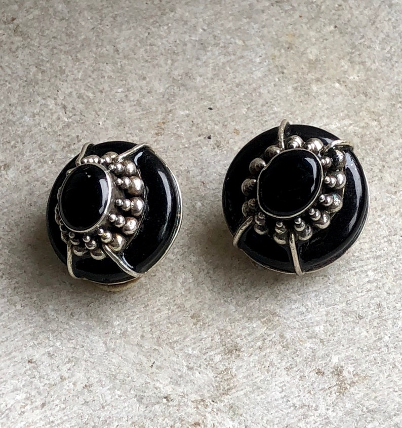 May include: A pair of black onyx earrings with silver accents. The earrings are round and have a beaded design around the edge.