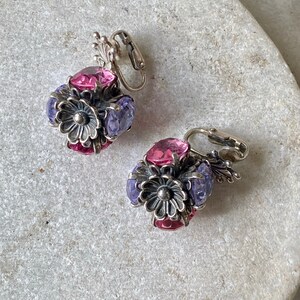 May include: A pair of silver tone clip-on earrings with pink and purple glass stones in a flower design.