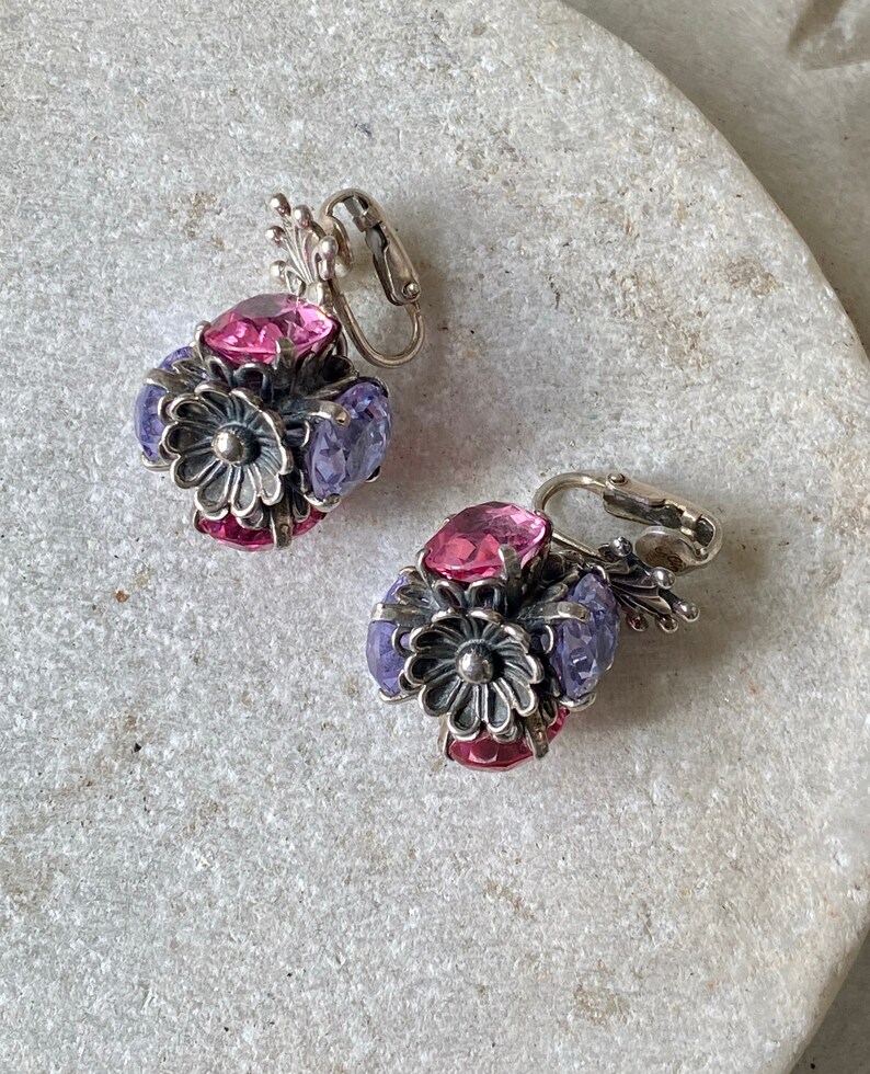 May include: A pair of silver tone clip-on earrings with pink and purple glass stones in a flower design.
