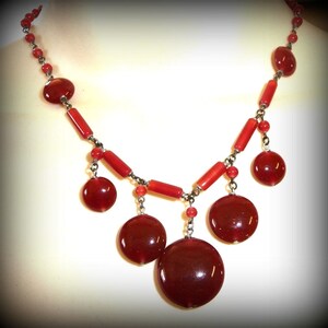 May include: A red beaded necklace with a silver chain and large, round red beads. The necklace has a dangling design with multiple strands of beads.