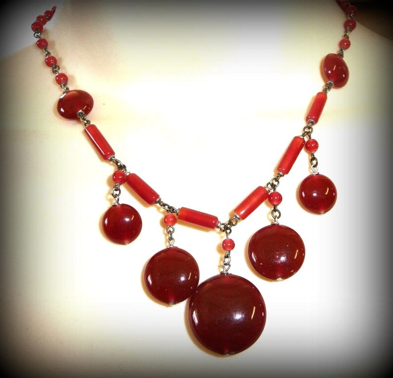 May include: A red beaded necklace with a silver chain and large, round red beads. The necklace has a dangling design with multiple strands of beads.