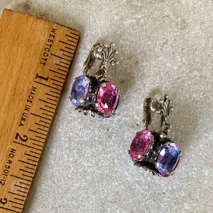 May include: A pair of silver clip-on earrings with pink and purple faceted stones. The earrings have a delicate floral design.