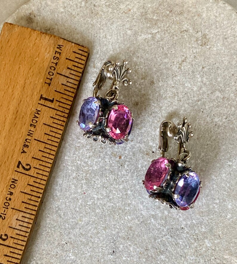 May include: A pair of silver clip-on earrings with pink and purple faceted stones. The earrings have a delicate floral design.