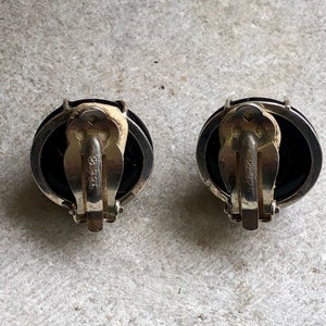 May include: A pair of black and silver clip-on earrings with a round, black stone. The earrings are marked with "925" on the back.