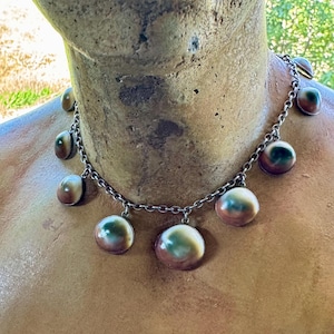 May include: A silver chain necklace with multiple round, iridescent shell pendants. The shells have a green, brown, and white color pattern.