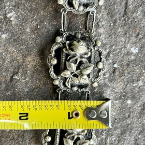 May include: A silver chain bracelet with three rose-shaped charms. The bracelet is approximately 2 inches long.