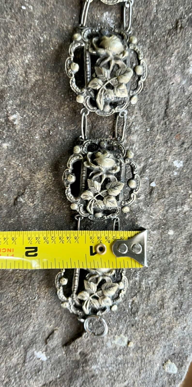 May include: A silver chain bracelet with three rose-shaped charms. The bracelet is approximately 2 inches long.
