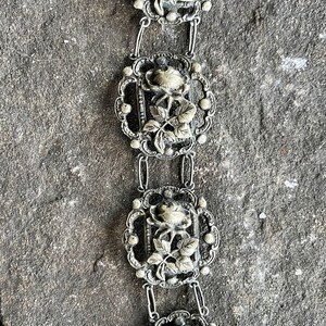 May include: A silver bracelet with four ornate rose-shaped links. Each link features a detailed rose with leaves and a delicate filigree design.