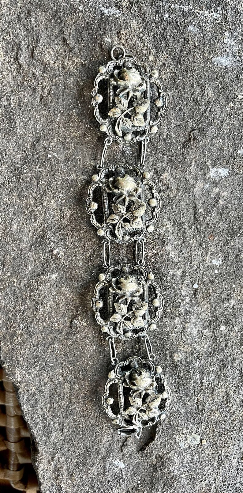 May include: A silver bracelet with four ornate rose-shaped links. Each link features a detailed rose with leaves and a delicate filigree design.