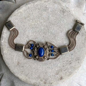 May include: A silver bracelet with a large blue gemstone surrounded by smaller blue beads and intricate silver detailing.