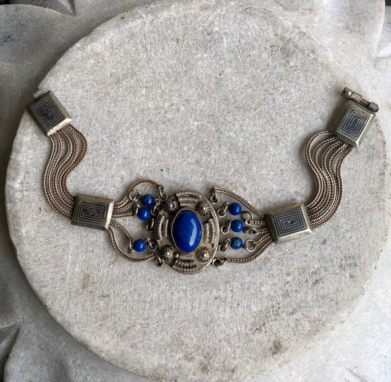 May include: A silver bracelet with a large blue gemstone surrounded by smaller blue beads and intricate silver detailing.