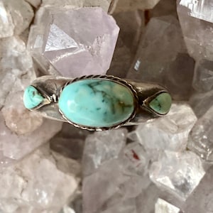 Puede incluir: Un anillo de plata con tres piedras turquesa. La piedra más grande es de forma ovalada y las dos piedras más pequeñas son de forma de lágrima.