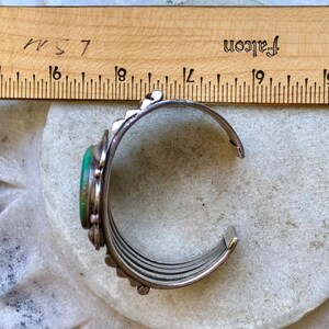 Puede incluir: Un brazalete de plata con una piedra turquesa y un dise&ntilde;o decorativo. El brazalete est&aacute; hecho de varias bandas que est&aacute;n conectadas entre s&iacute;.