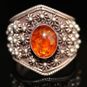 May include: A silver ring featuring an orange amber gemstone set within a floral design.