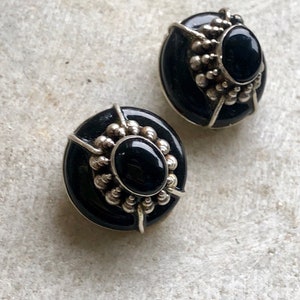 May include: A pair of black onyx earrings with silver settings. The earrings are oval shaped and have a beaded design around the onyx stones.