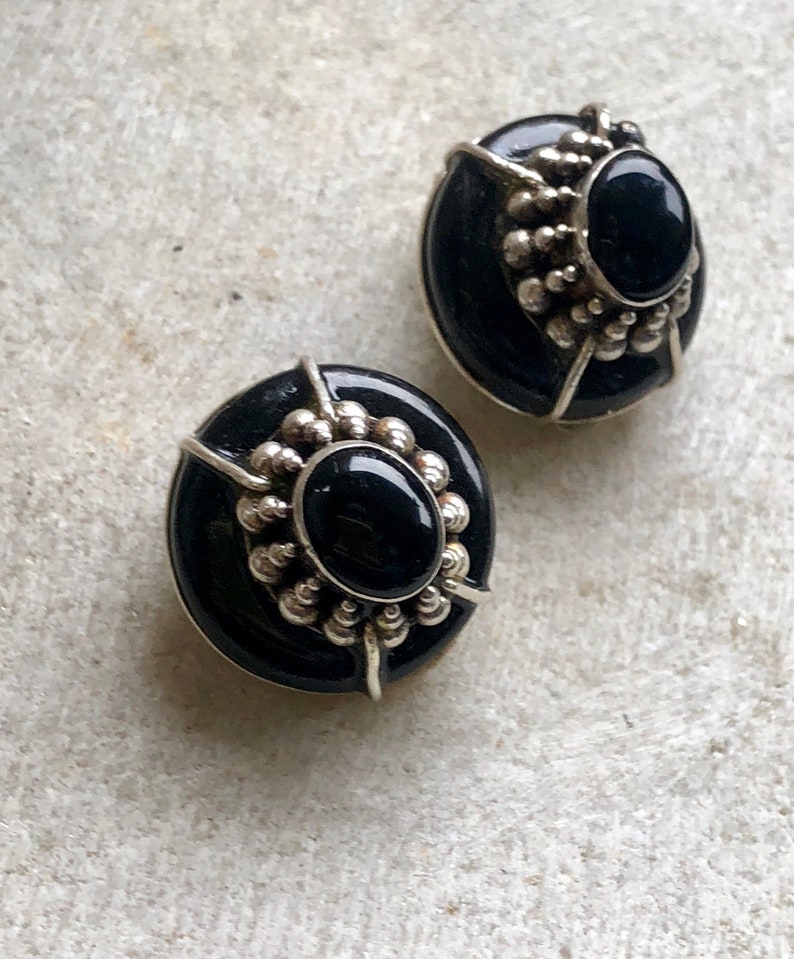 May include: A pair of black onyx earrings with silver settings. The earrings are oval shaped and have a beaded design around the onyx stones.