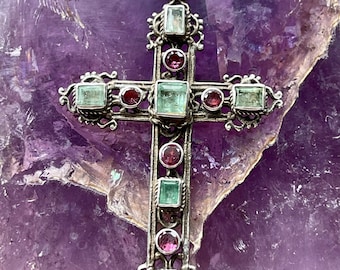 May include: A silver cross pendant with green and pink gemstones. The cross is ornate and has a detailed design.