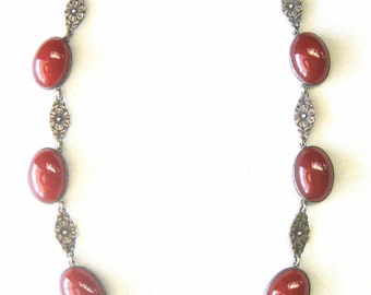 May include: A silver necklace with a floral design and red carnelian stones.