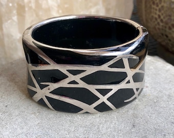 May include: Black bangle bracelet with a silver geometric design.