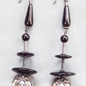 May include: A pair of dangle earrings with black onyx beads and clear crystal balls. The earrings have silver hooks and are suspended from a silver chain.
