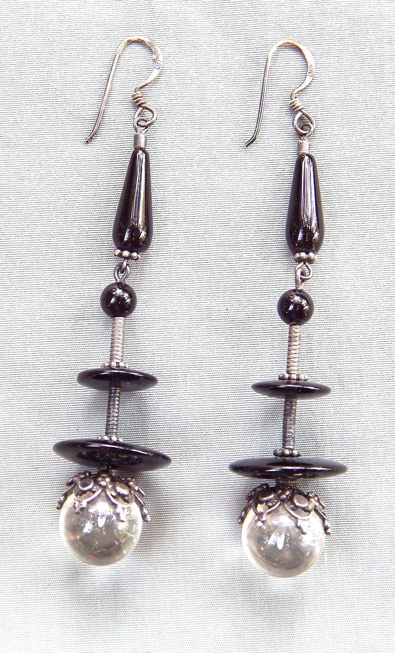 May include: A pair of dangle earrings with black onyx beads and clear crystal balls. The earrings have silver hooks and are suspended from a silver chain.
